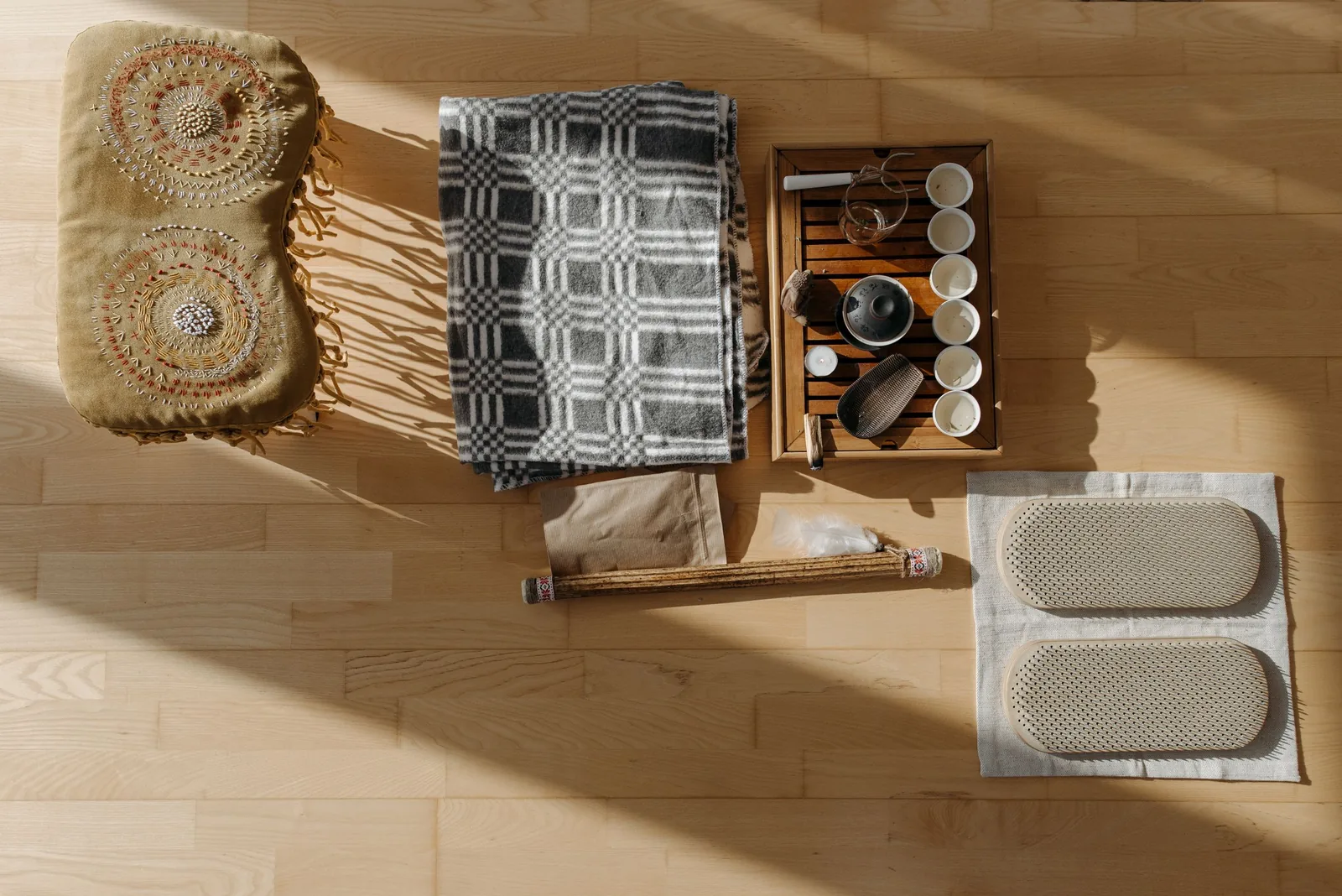 Van bovenaf: een meditatiekussen, een opgevouwen deken en een theepot met kopjes op een houten vloer